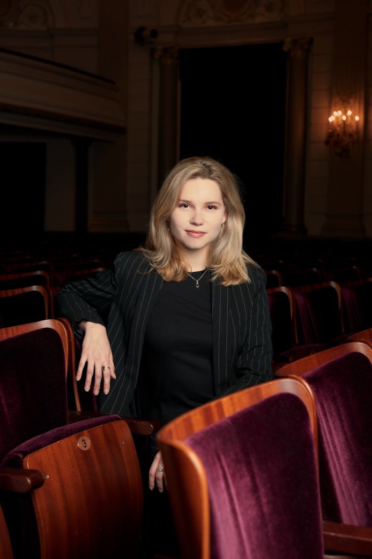 Among the theatre seats, resting an arm on a chair back